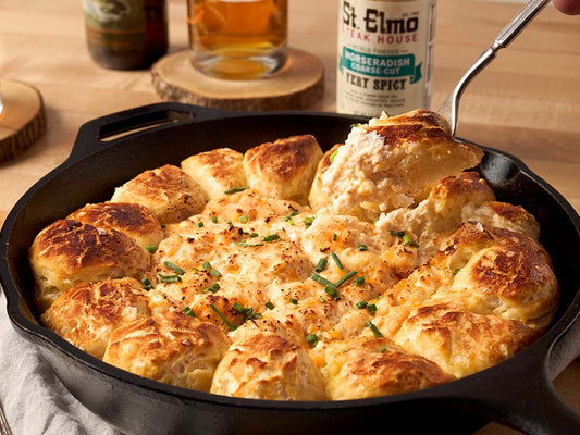 Pull-apart pretzel ring with creamy beer cheese dip topped with chives and served in a cast iron skillet.