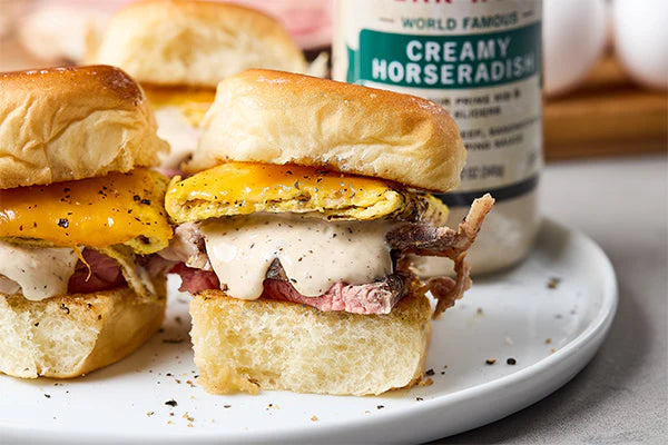 Breakfast sliders with roast beef, fried eggs, melted cheddar cheese, and creamy horseradish sauce on soft buns.