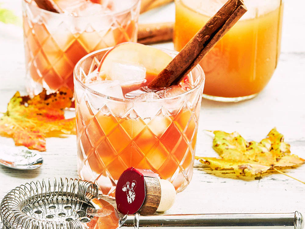 Apple cider bourbon cocktail served over ice with apple slices and a cinnamon stick garnish in a crystal rocks glass.