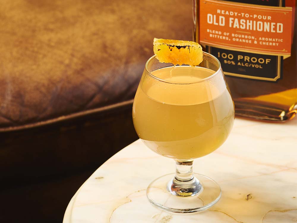 Hot Old Fashioned toddy cocktail garnished with a candied orange slice beside a bottle of St. Elmo Ready-to-Pour Old Fashioned.