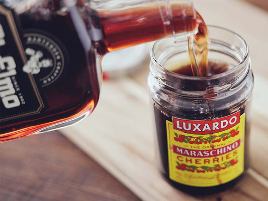 St. Elmo Cherry Vanilla Bourbon being poured into a jar of Luxardo maraschino cherries to make bourbon-soaked drunken cherries.