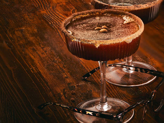 Espresso martini with a brown sugar caramel rim served in a coupe glass, topped with espresso beans on a dark wood table.