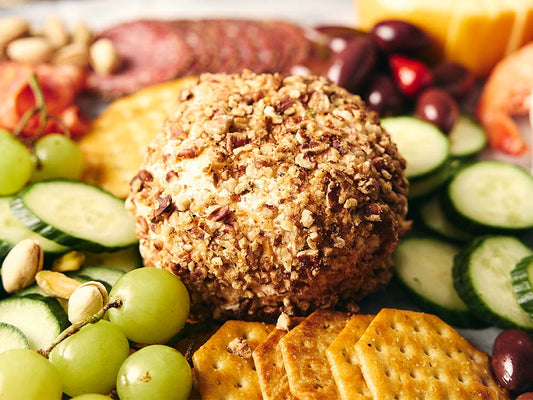 Horseradish cheese ball coated in chopped pecans surrounded by crackers, cucumbers, grapes, and charcuterie board accompaniments.