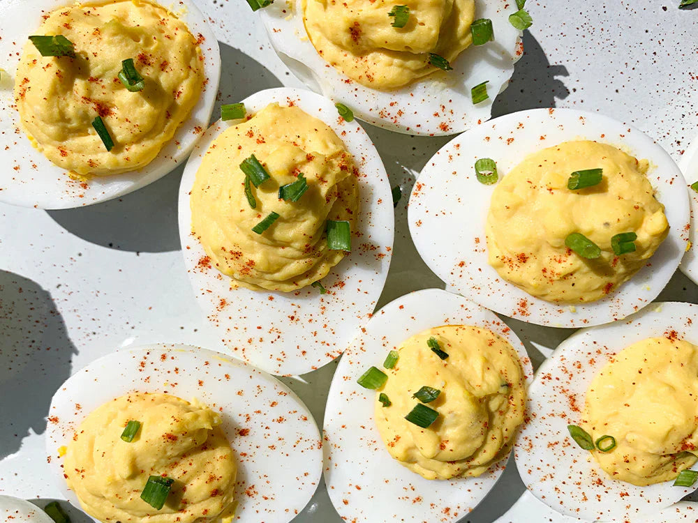 Creamy horseradish deviled eggs garnished with chopped chives and paprika on a white serving platter.