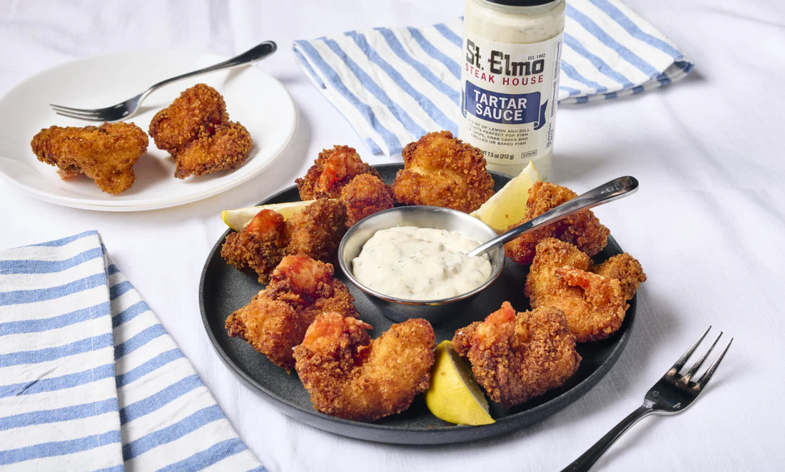Crispy fried shrimp served on a platter with lemon wedges and creamy tartar sauce, alongside a bottle of tartar sauce for dipping.
