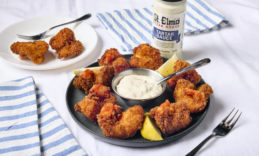 Crispy fried shrimp served on a platter with lemon wedges and creamy tartar sauce, alongside a bottle of tartar sauce for dipping.