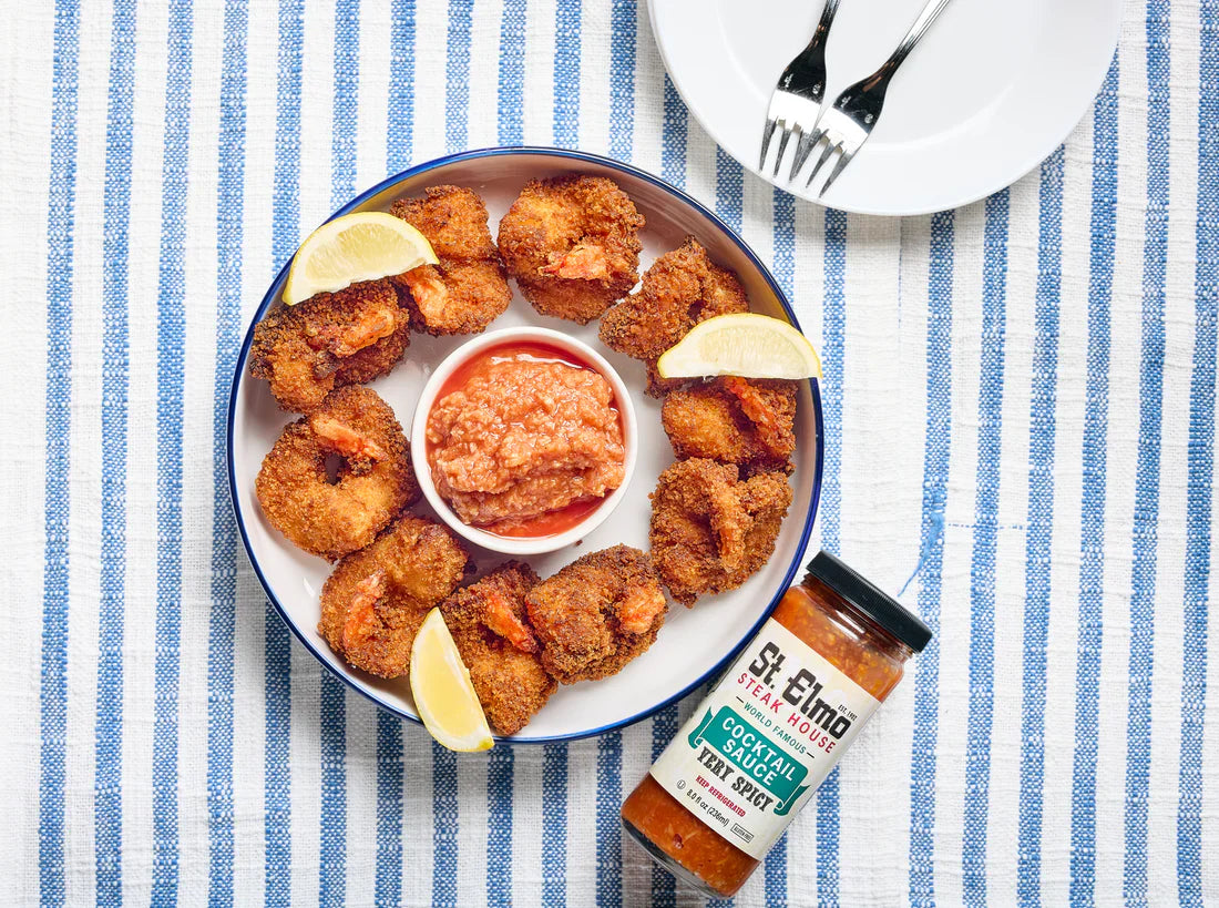 Crispy fried shrimp arranged on a platter with lemon wedges and spicy cocktail sauce, served alongside a jar of cocktail sauce.