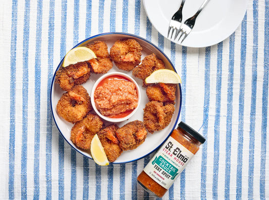 Crispy fried shrimp arranged on a platter with lemon wedges and spicy cocktail sauce, served alongside a jar of cocktail sauce.