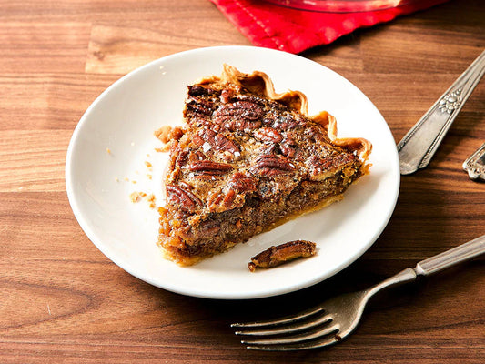 Slice of bourbon pecan pie with a flaky crust and toasted pecan topping served on a white plate.