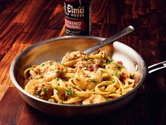 Creamy seafood pasta with blackened shrimp and linguine garnished with parsley, served in a skillet beside blackened seasoning.