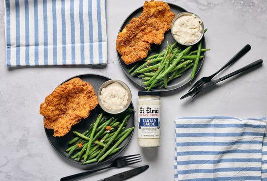Crispy coconut-panko grouper fillets served with sautéed green beans and tartar sauce on black plates.