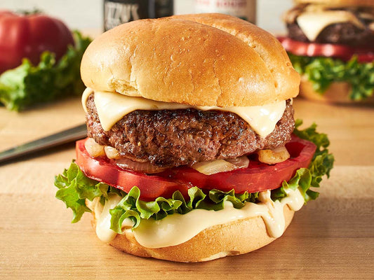 Steak burger topped with melted cheese, lettuce, tomato, grilled onions, and creamy sauce on a toasted bun.