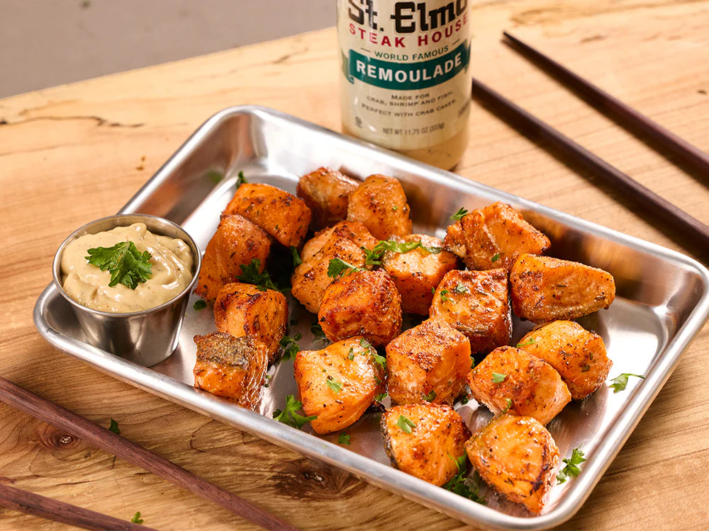 Blackened salmon bites served with creamy remoulade dipping sauce on a metal tray, garnished with fresh parsley.