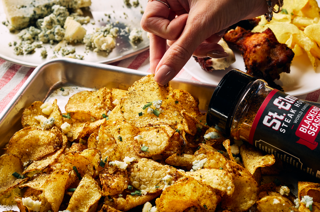 Crispy blackened potato chips seasoned with St. Elmo Blackened Seasoning and topped with blue cheese crumbles and chives, served warm in a metal tray.
