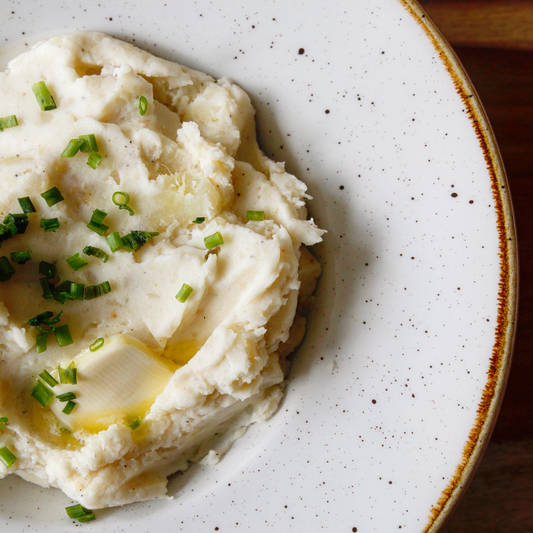 Creamy mashed potatoes topped with butter and fresh chives served in a white bowl.