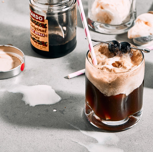 Bourbon cola float topped with vanilla ice cream and cherries served in a glass with a striped straw.