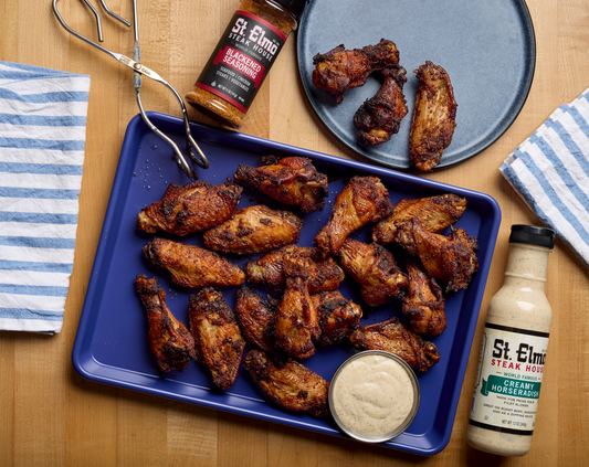 Crispy baked blackened chicken wings seasoned with St. Elmo Blackened Seasoning and served with creamy horseradish dipping sauce on a blue tray.